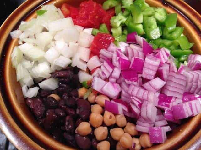 Chopped red onion, white onion, green peppers, and cooked beans in a brown bowl.