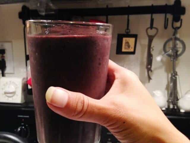 A hand holding a glass filled with blueberry kale smoothie.