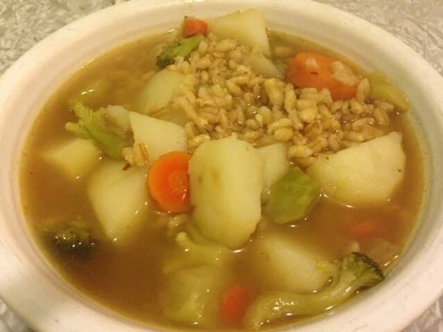 Small white bowl of vegetable barley soup containing carrots and potatoes.