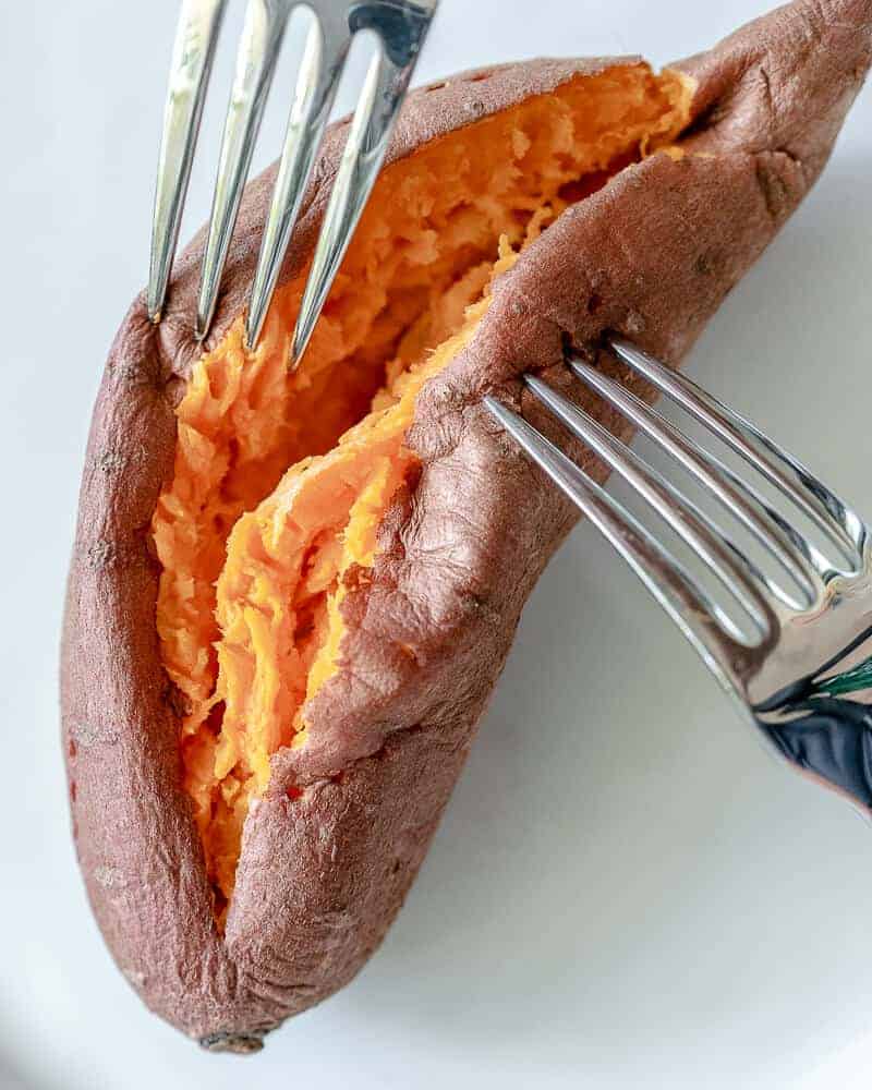 sweet potato cut in half on white plate with forks helping to split the halves