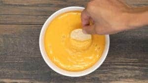 A chip being dipped into a bowl of vegan nacho cheese.