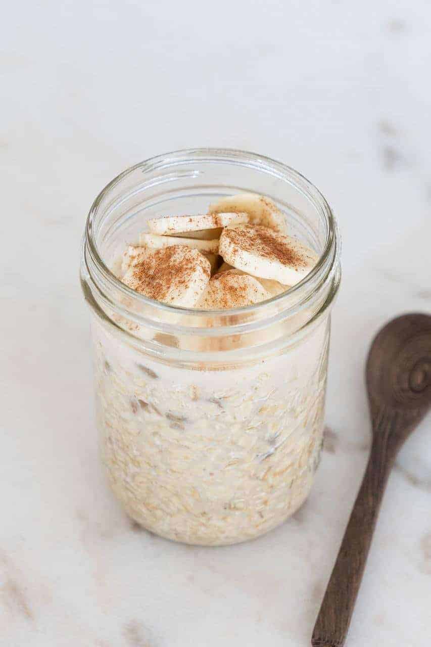 Pint Mason jar filled with overnight oats topped with sliced bananas and cinnamon.