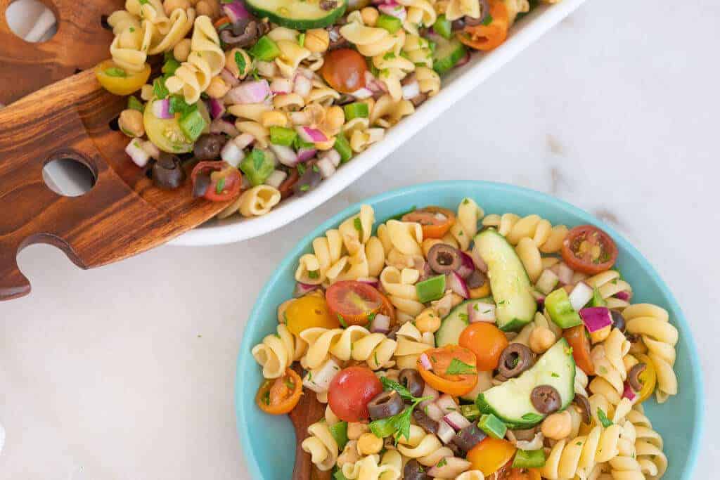 finished pasta salad in white tray and blue bowl against a white background