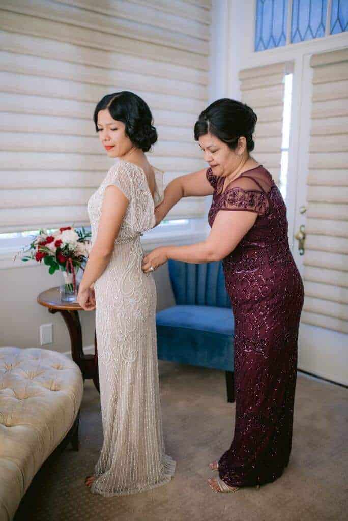 Bride's dress being zipped up by her mom.