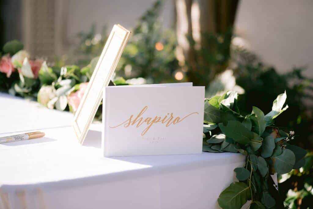 A wedding guest book and gold pens waiting on a white table.