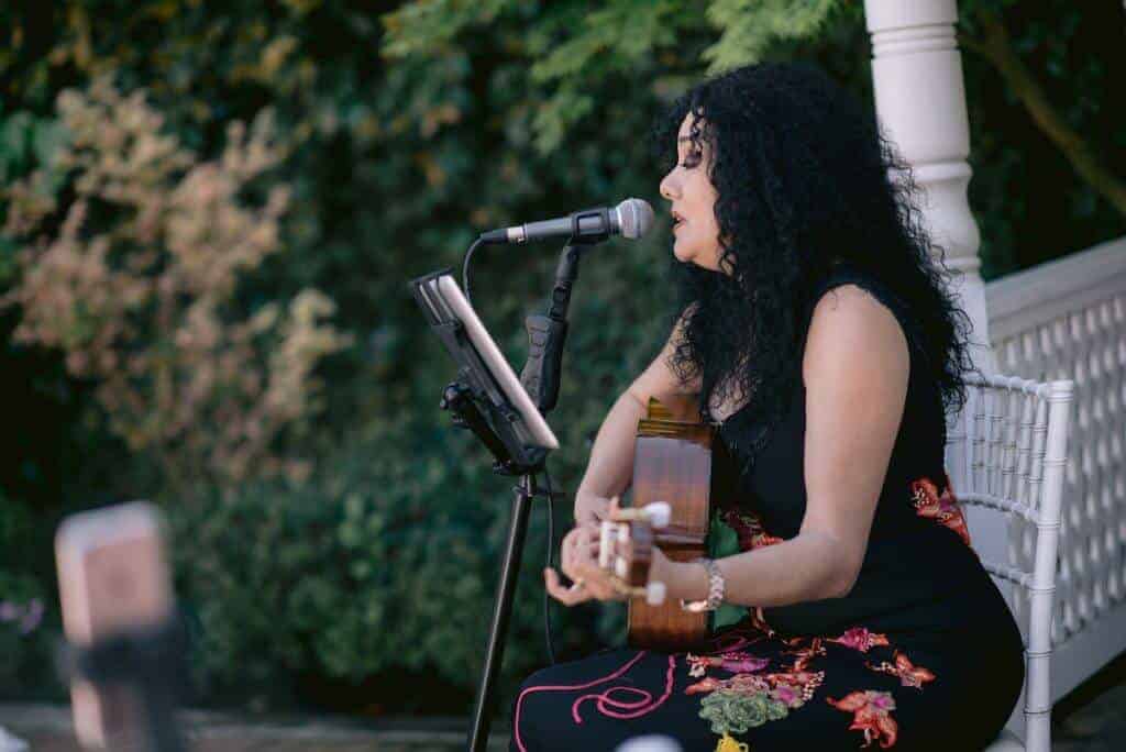 Woman playing a guitar and singing into a mic.