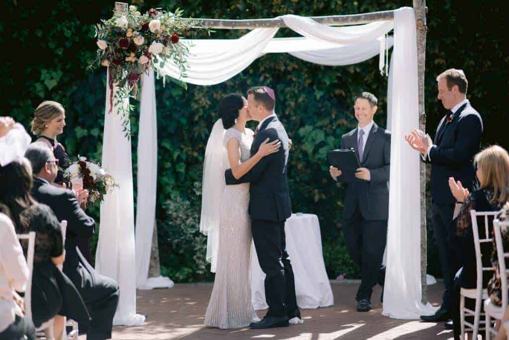 Bride and groom kissing under a chuppah.
