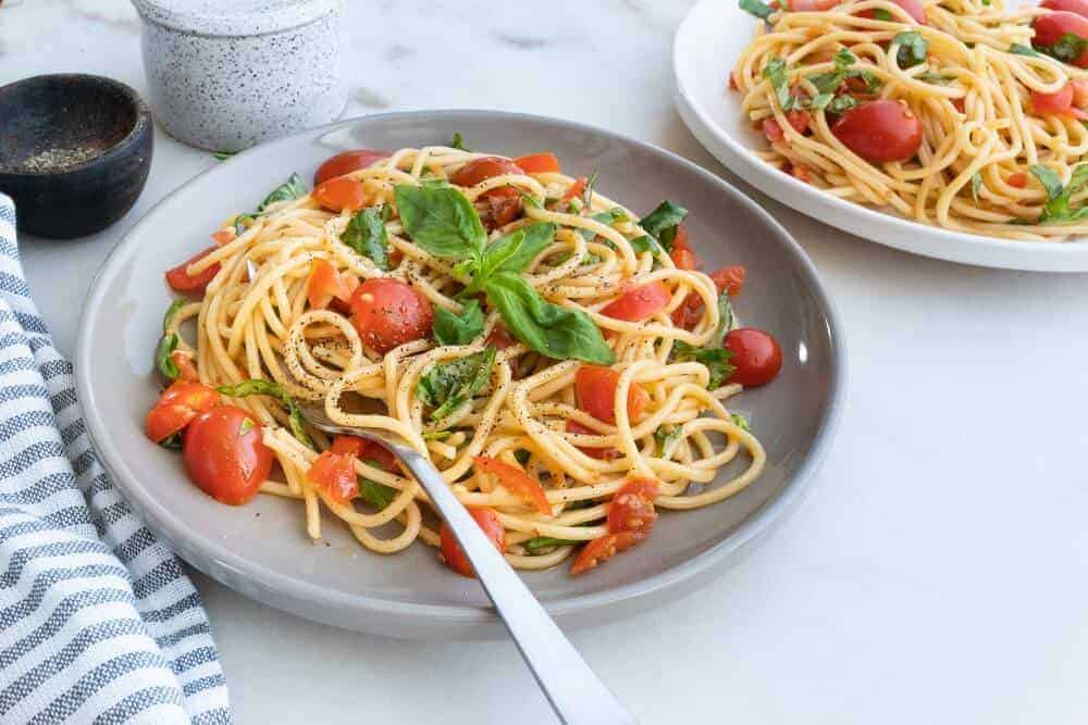 finished plate of Simple Pasta with Tomatoes and Basil on a gray plate on top of a white surface