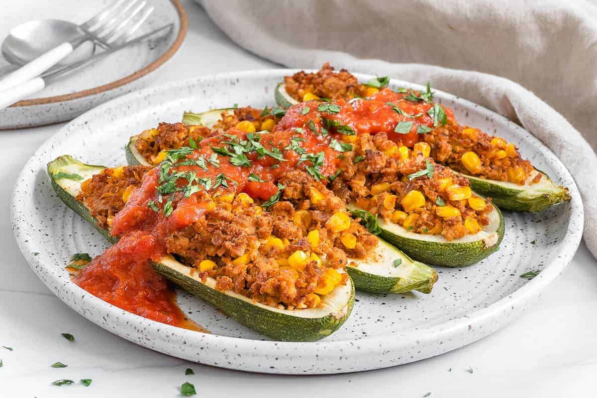 4 finished tex mex zucchini boats on a white plate with a white background