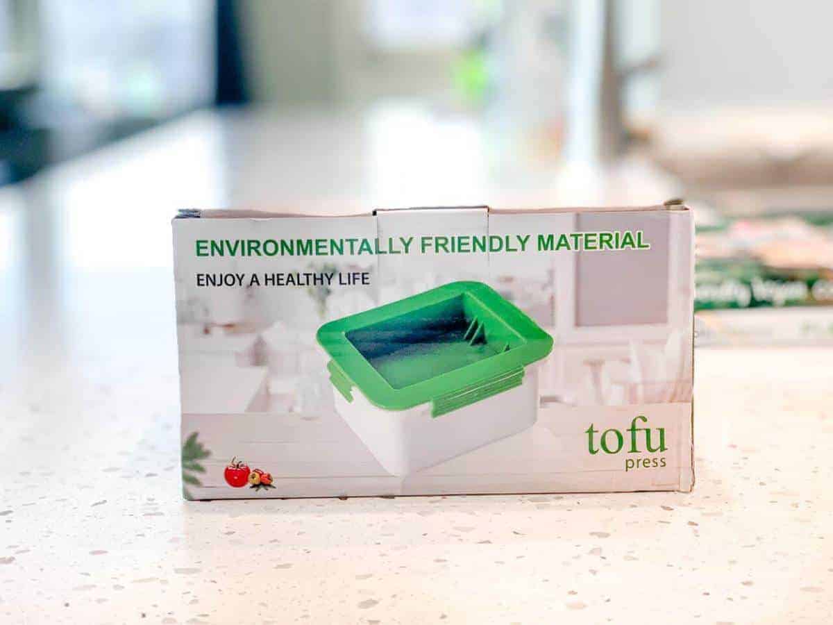 A tofu press in a box on a marble counter.