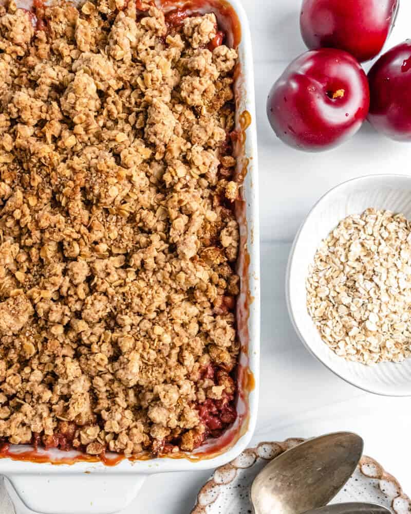 vegan plum crisp with ingredients in a white background