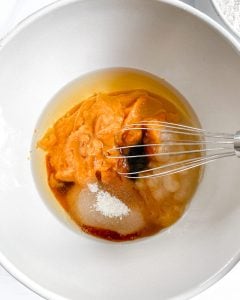 process of wet ingredients for pumpkin bread in white bowl against white background