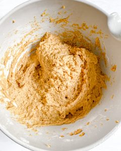process of wet ingredients being mixed for pumpkin bread in white bowl against white background
