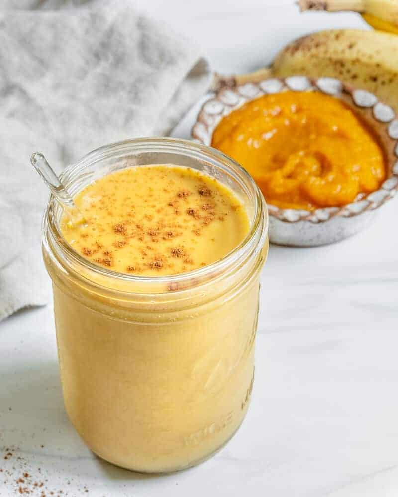 Pumpkin Pie Smoothie in glass jar on white surface on with ingredients in the background