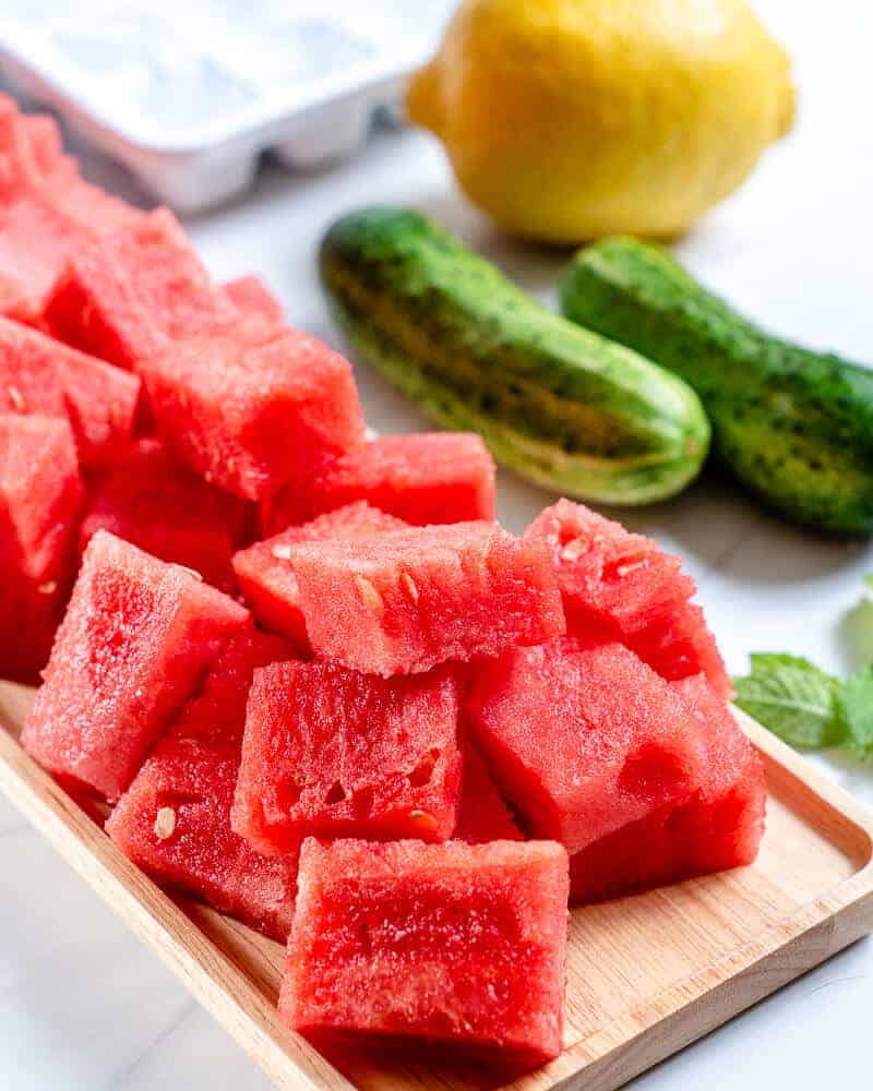 watermelon cooler process of sliced watermelon on a wood tray with 2 zucchinis and 1 lemon and 1 ice tray in a white background 