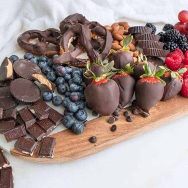 completed charcuterie board with chocolates and strawberries and other vegan candies spread out on a board against a white background