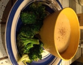 Bowl of creamy cauliflower soup next to roasted broccoli.