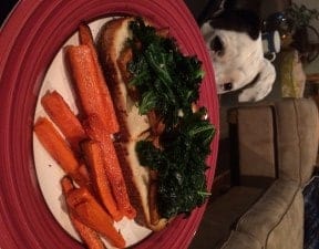 An open faced tofu and kale sandwich with a side of roasted carrots on a plate.