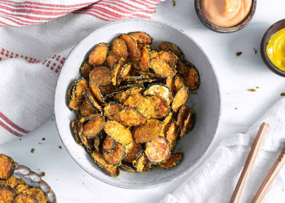 cooked cheesy zucchini chips in white bowl against a white background