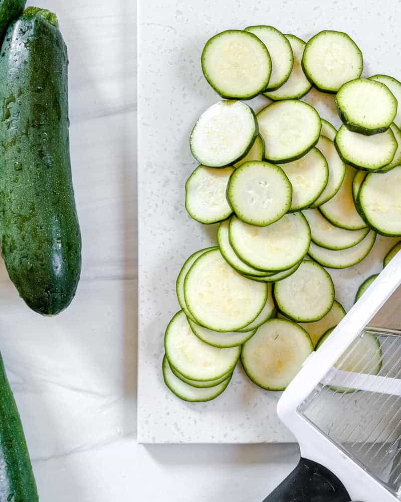 prepared cut up zucchini on a cutting board with whole zucchinis in the background