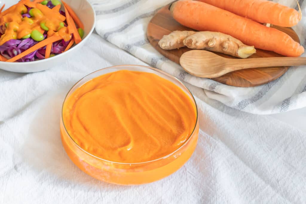 japanese carrot ginger salad dressing in a galss bowl with carrot ingredients in a white background