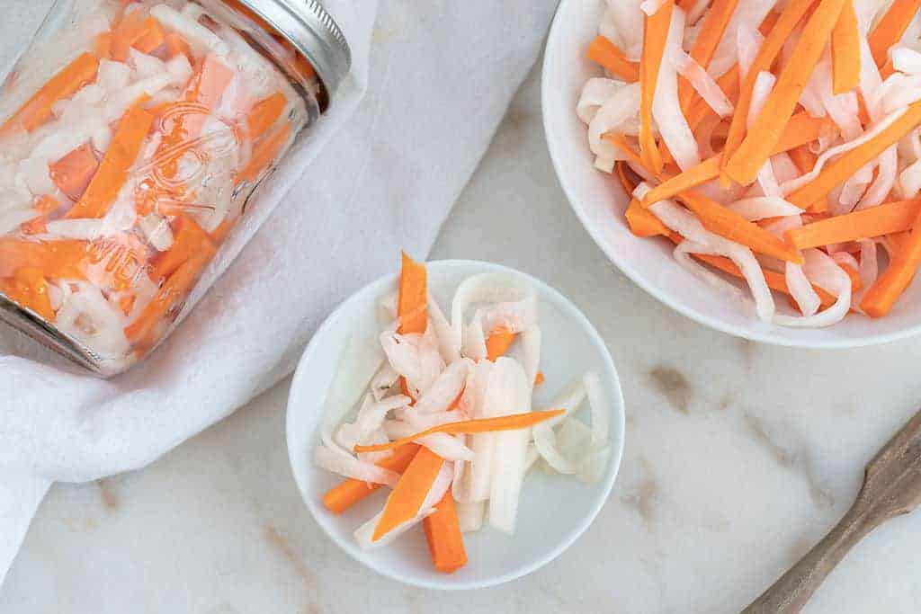 finished pickled carrots in a jar and in two separate bowls against a white background