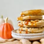 completed Vegan Pumpkin Waffles stacked on top of one another on a white plate with a pumpkin in the background