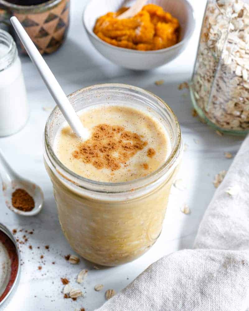 finished Pumpkin Pie Overnight Oats in a glass jar with a spoon inside with various ingredients in the background
