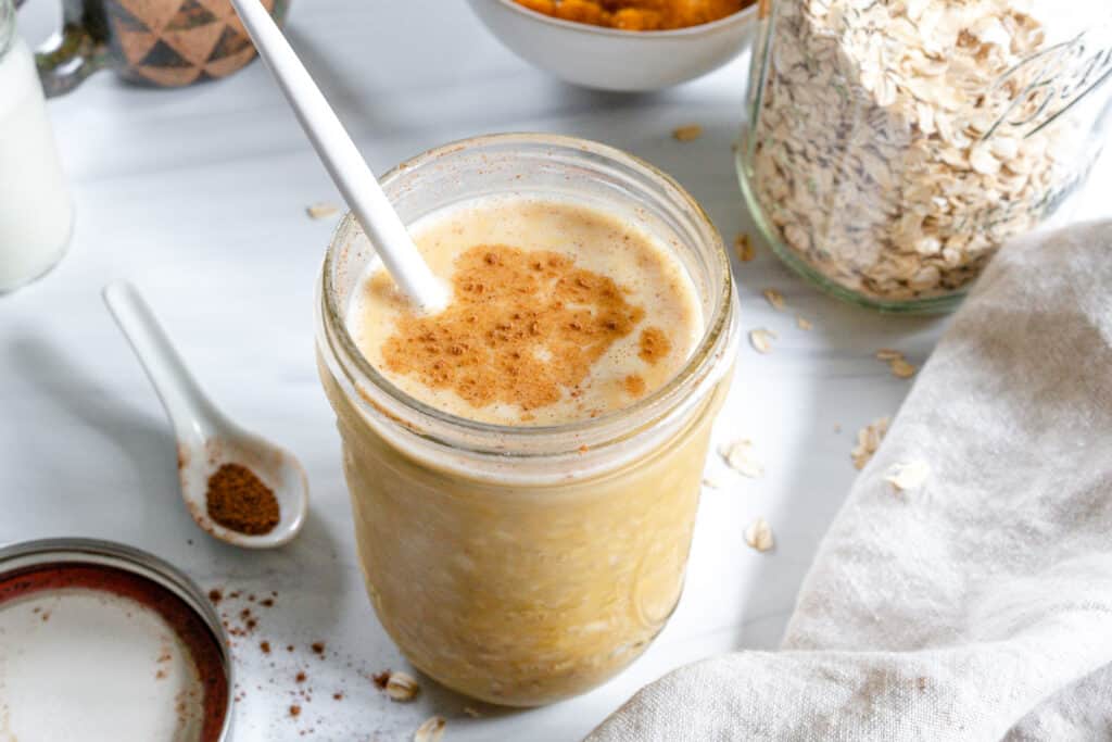 finished Overnight Pumpkin Pie Oats in a glass jar with ingredients in the background 