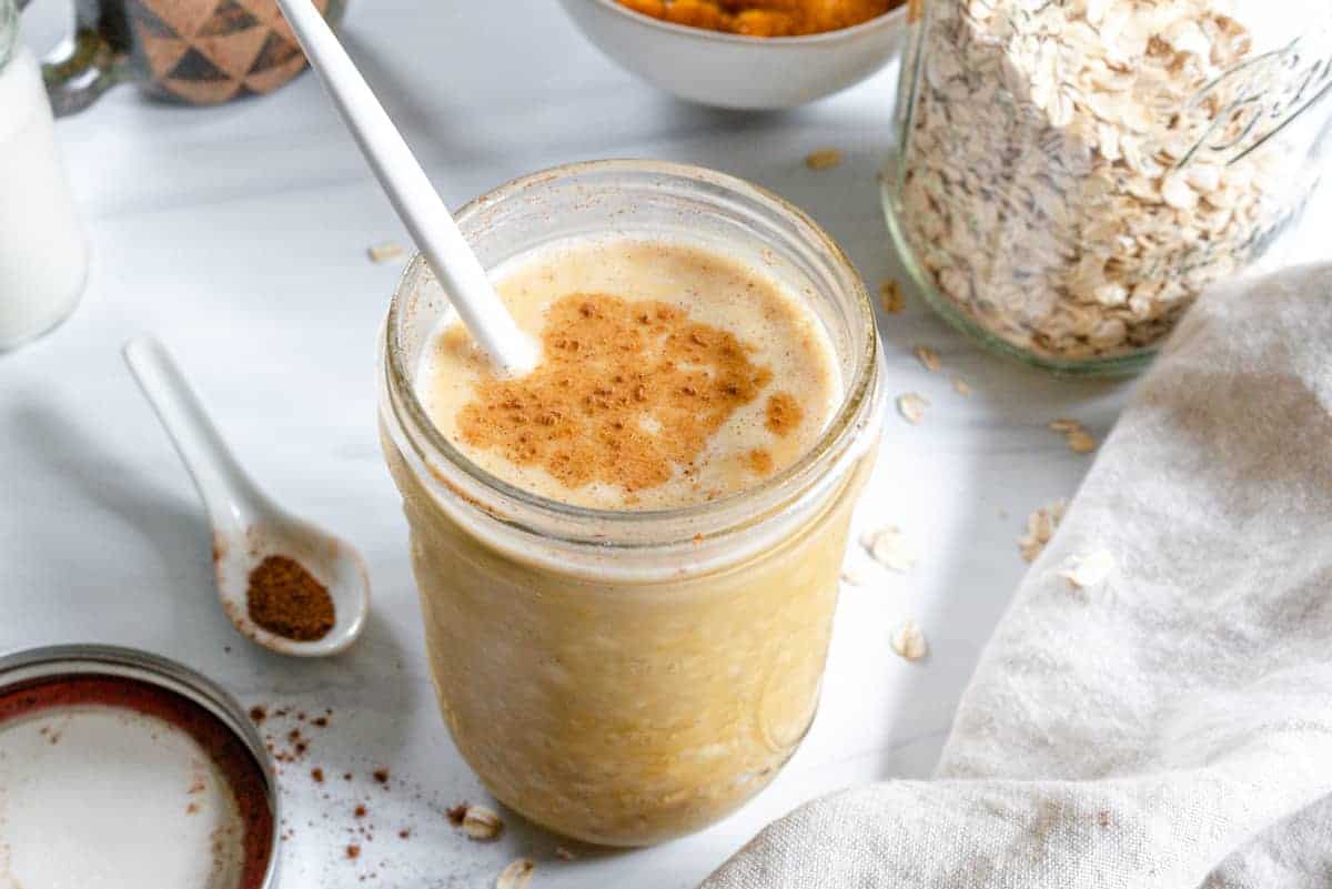 finished Pumpkin Pie Overnight Oats in a glass jar with a spoon inside with various ingredients in the background