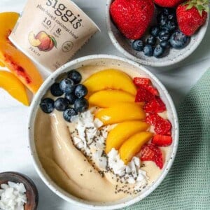 finished smoothie bowl topped with fruit in white bowl with yogurt and fruits scattered against a white background