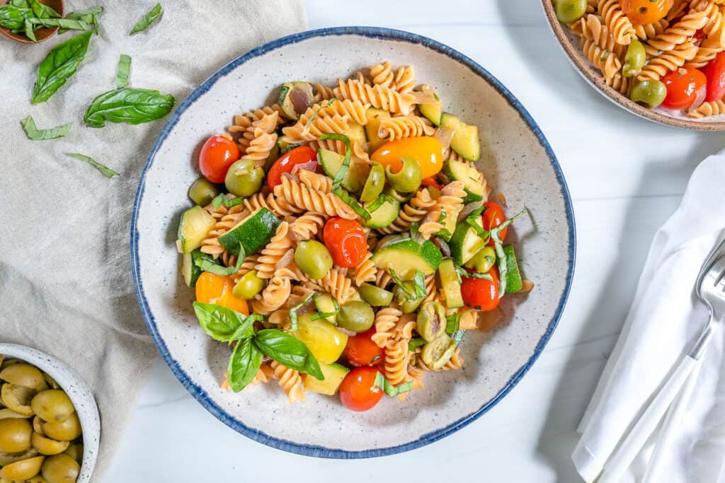 finished summertime pasta in a white plate with ingredients spread out in the background