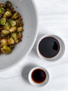 cooked brussels sprouts in a white bowl with wet ingredients in the background