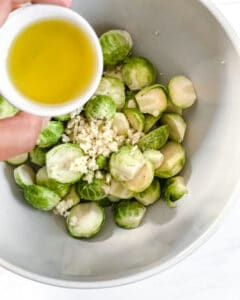 brussels sprouts in a white bowl with dressing about to be poured into the bowl