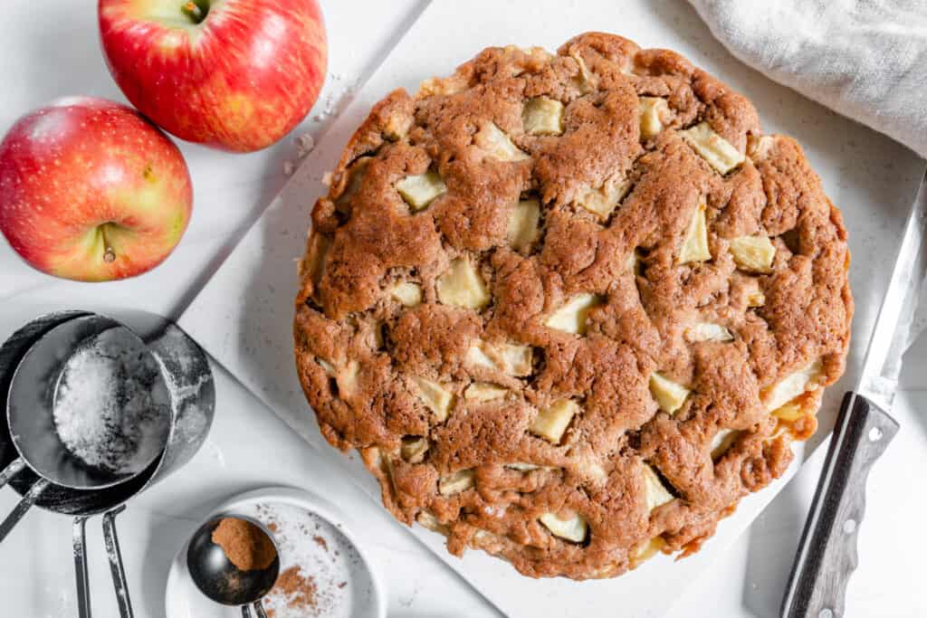 finished apple cake with 2 apples and measuring tools against a white background