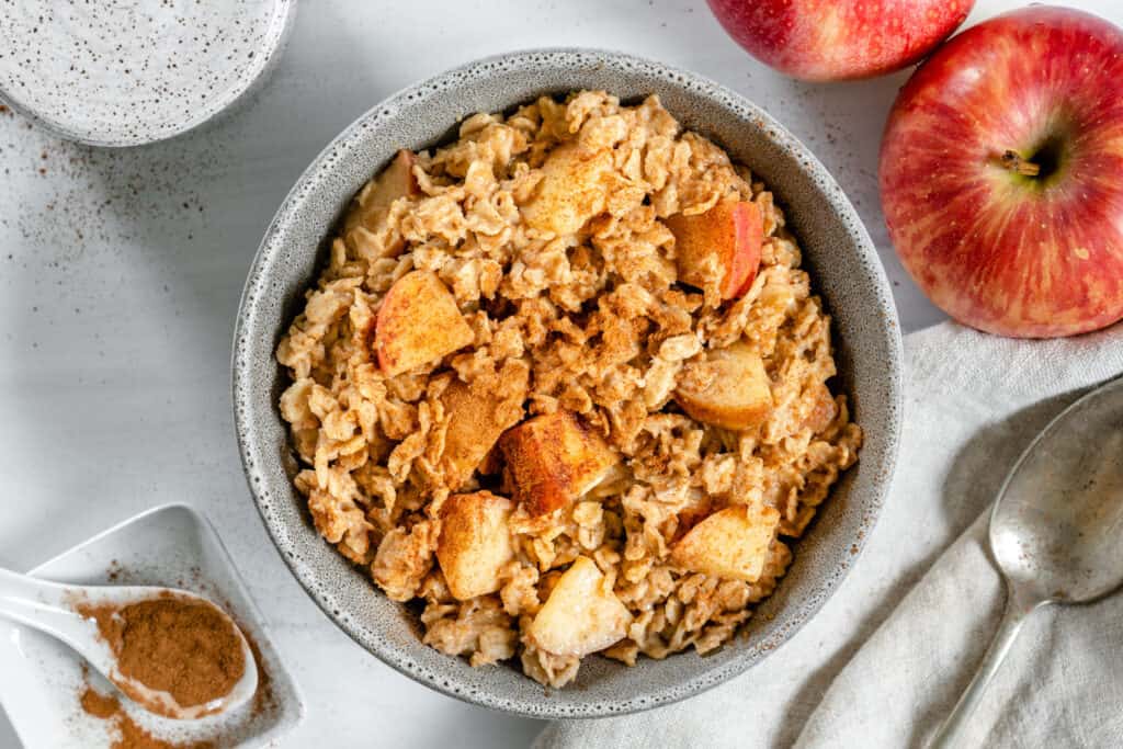 finished apple cinnamon oatmeal in a bowl with ingredients in a white background