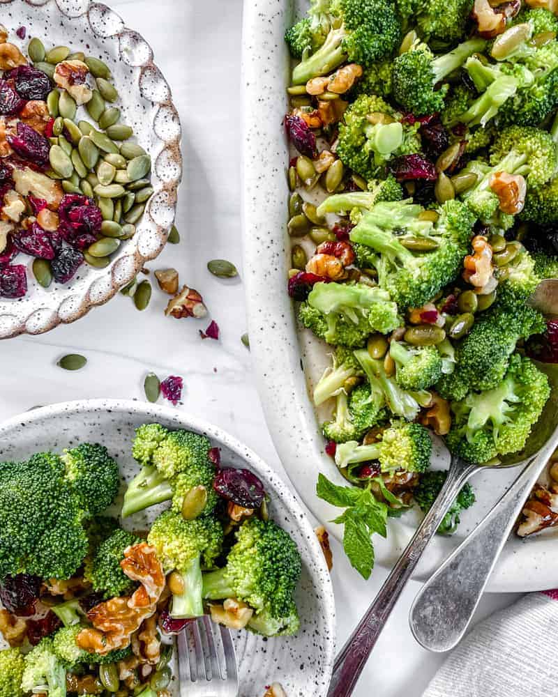 Vegan Broccoli Salad in a white dish against a white background with small plates of the salad in the background