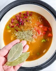 process of cooking Vegan Minestrone Soup in pot and adding herbs