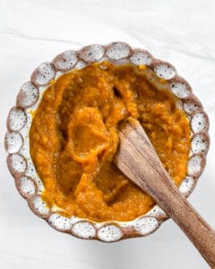 stuffed dates process showing the mixing of the pumpkin mixture in a white bowl with a wooden spoon against white background