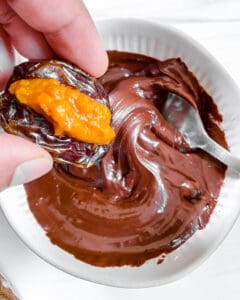 stuffed dates process showing date being dipped in melted chocolate in white bowl