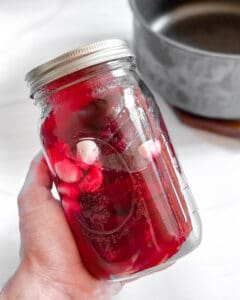 A hand holding a quart mason jar with sliced beets and their pickling liquid.