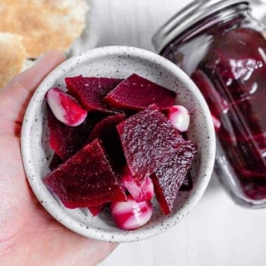 completed Small Batch Pickled Beets in a small bowl and mason jar against a white. background with several ingredients in the background