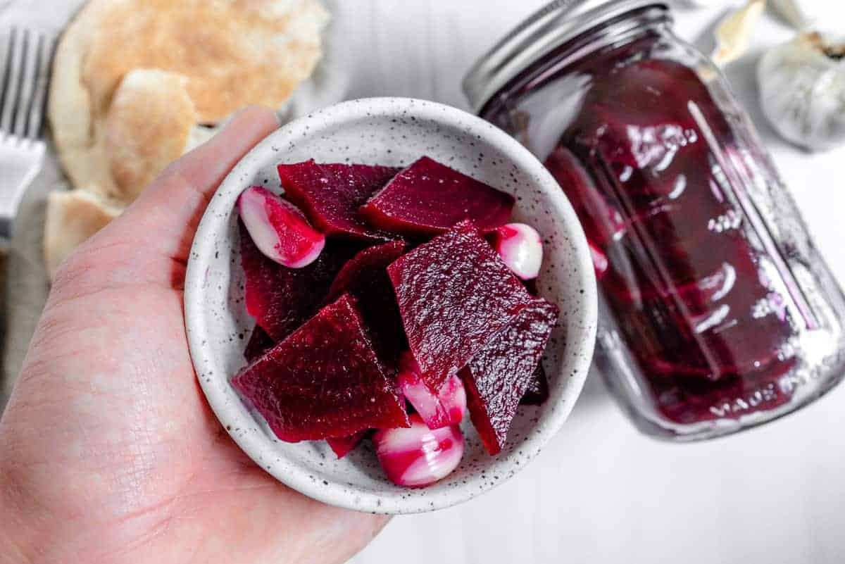 A hand holding a small bowl of pickled beets.