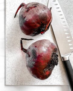 Knife and two beets on a cutting board.