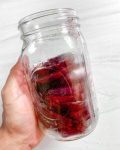 A hand holding a quart mason jar filled with sliced beets.