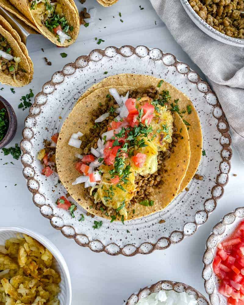Breakfast Tacos in a white plate with tacos and ingredients in the background against white surface