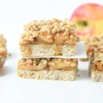 finished vegan apple bars stacked on each other with apples against a white background