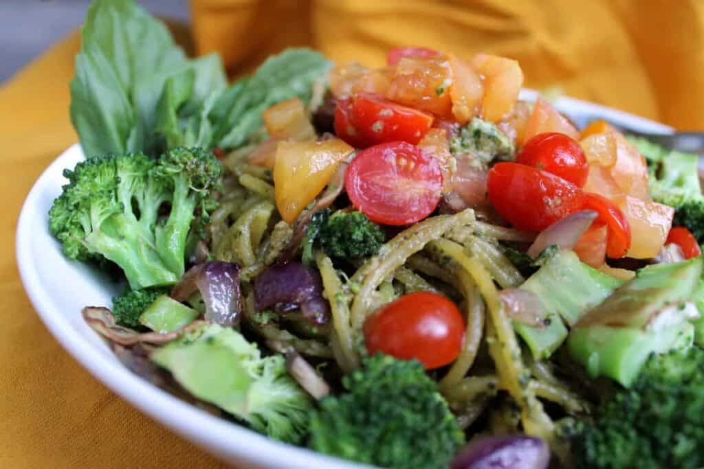 finished sunflower seed pesto in a white plate mixed iwth veggies against a dark background