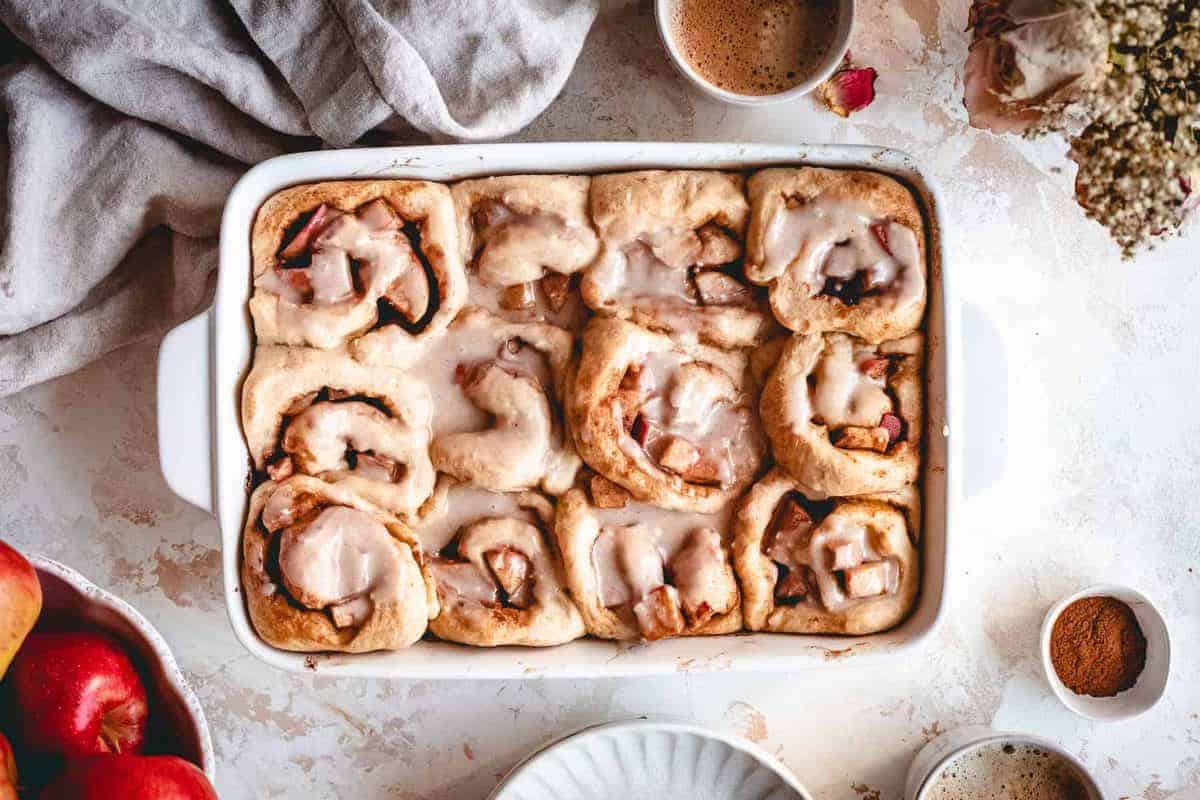 apple pie cinnamon rolls in tray with several ingredients in the background