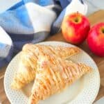 finished vegan apple turnovers on a white plate with apples and a towel in the background